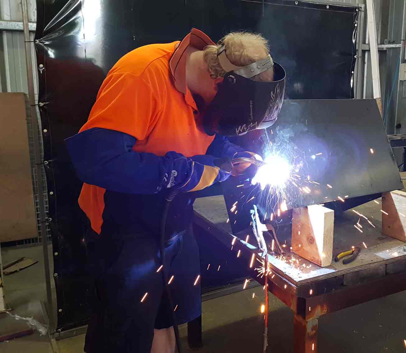 Man welding metal with protective face cover on.