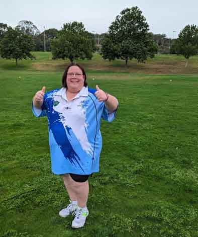 Woman in blue and white sports uniform, standing in a field with two thumbs up.
