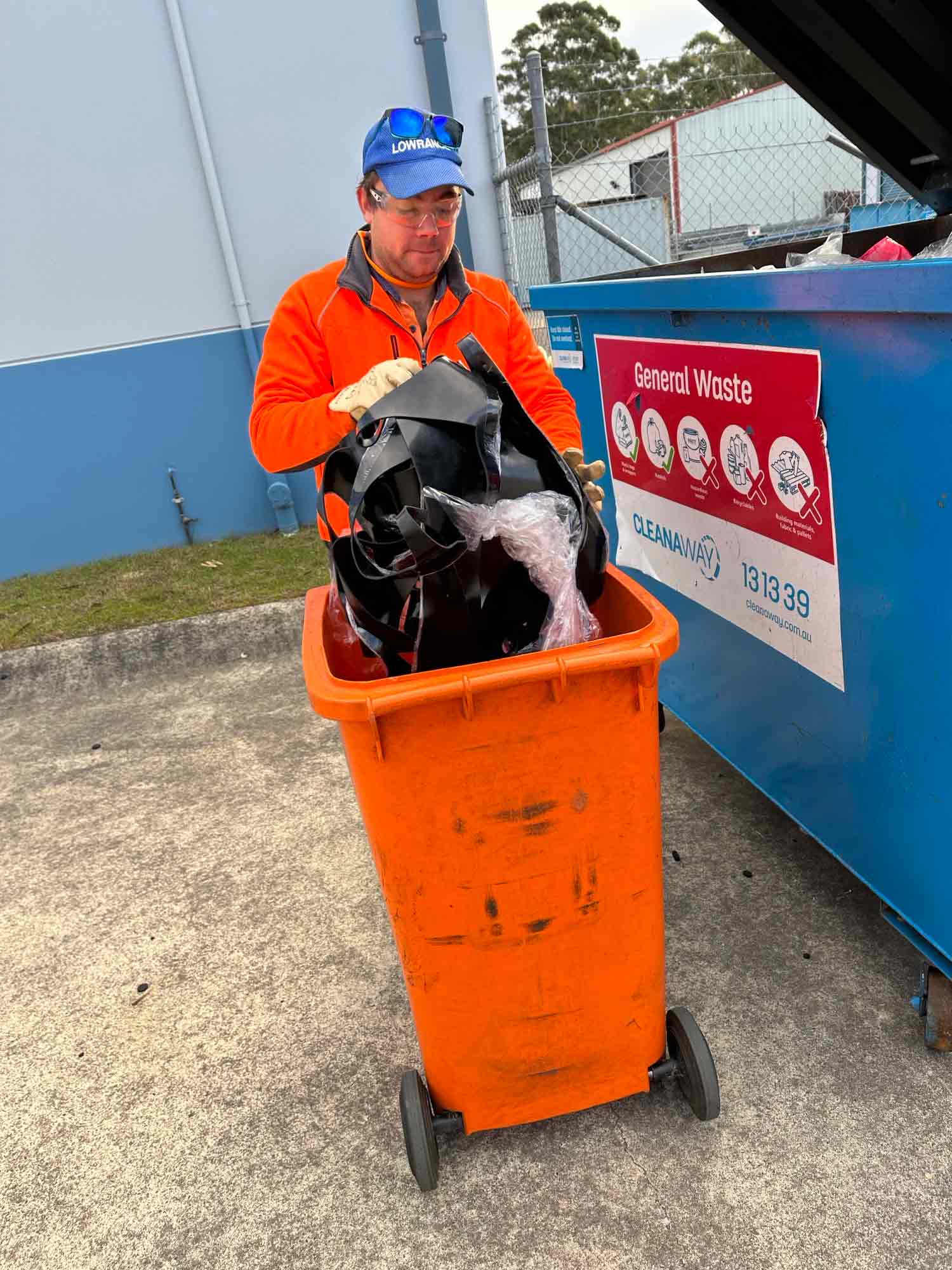 Man in high-vis throwing items from a wheelie bin into a dumpster.