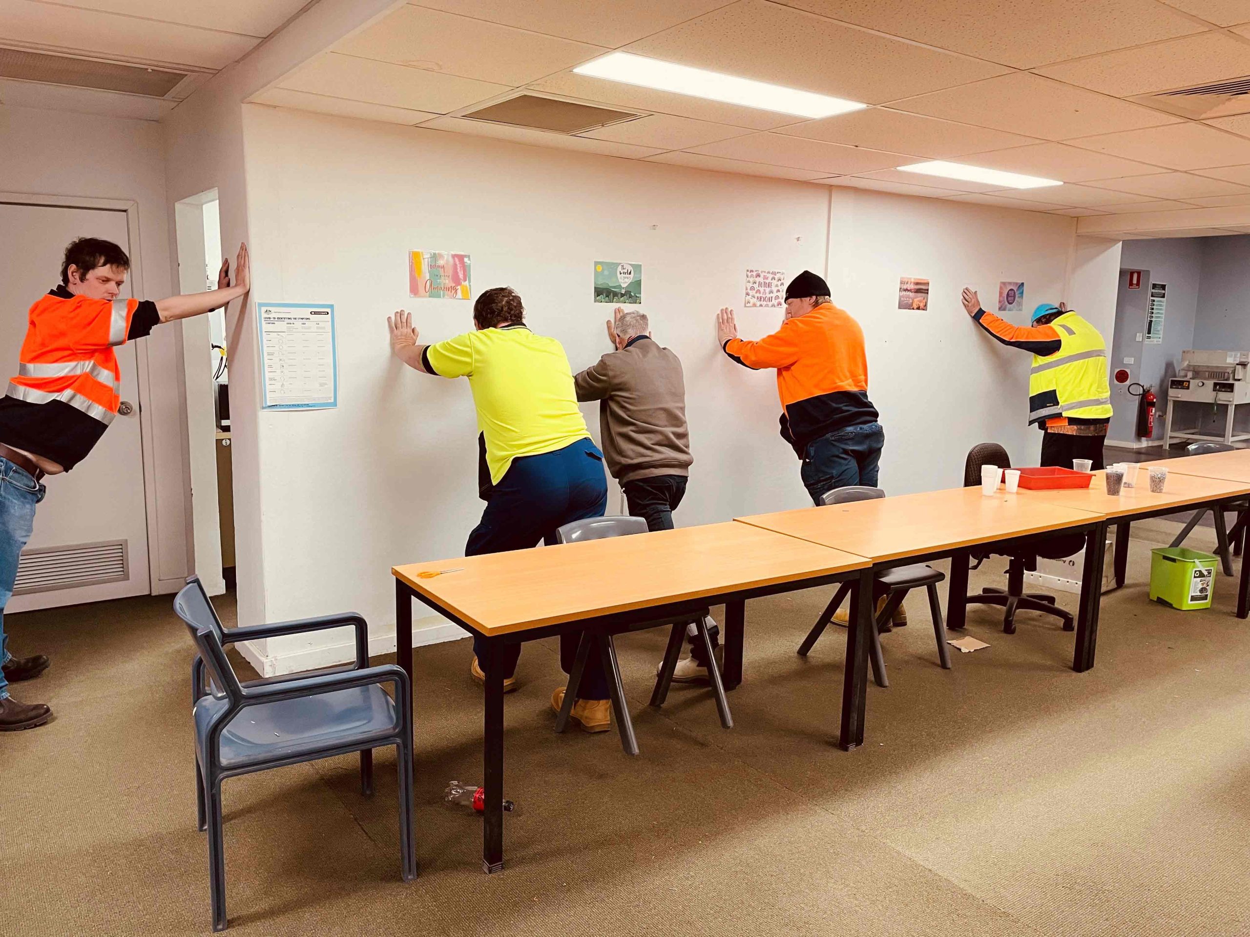 A line of men in high-vis stretching against a wall.